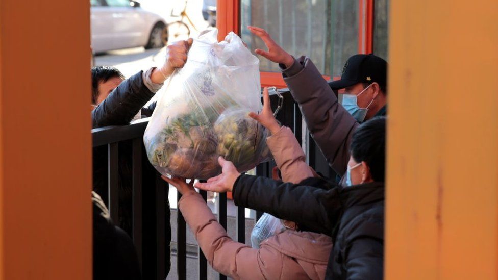 Residents receive daily necessities at the entrance of a residential community under lockdown on December 29, 2021 in Xi'an