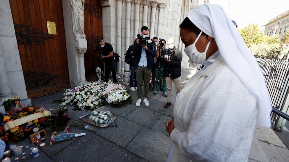 A nun prays in front of candles and flowers left in tribute to the victims of a knife attack at the Notre Dame church in Nice, France, October 30, 2020