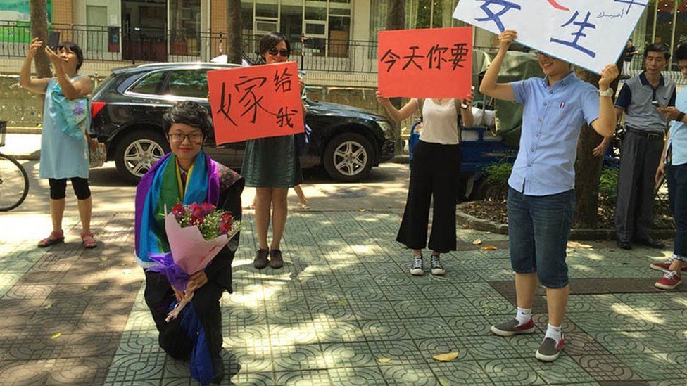 Jean Ouyang proposes to her girlfriend as the people in the background wave banners saying "Will you marry me today?"