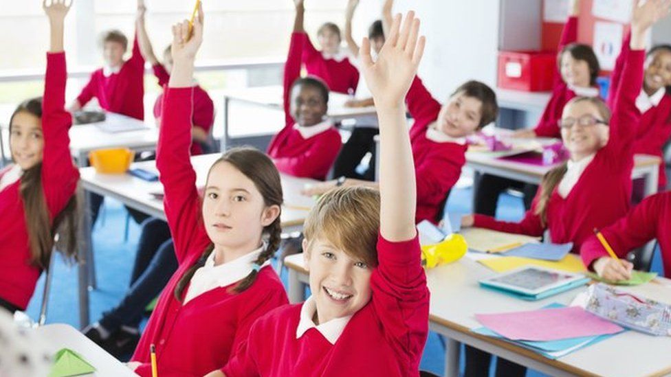Students with hands raised in classroom - stock photo