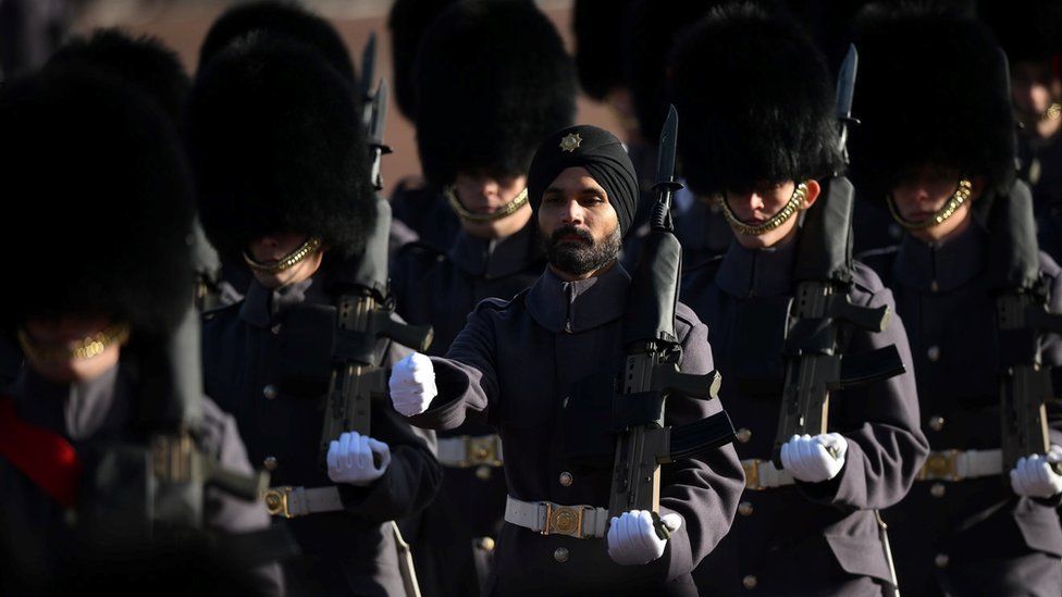 Soldiers dressed in dark clothing march along with guns in hands.