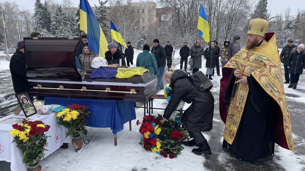 Imagem de pessoas reunidas em torno de um caixão no funeral de Denys Sosnenko