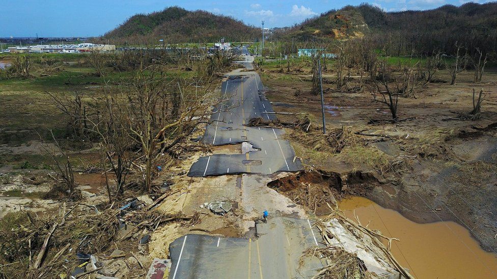 A man rides his bicycle through a damaged road in Toa Alta, west of San Juan, Puerto Rico, on September 24, 2017 following the passage of Hurricane Maria.