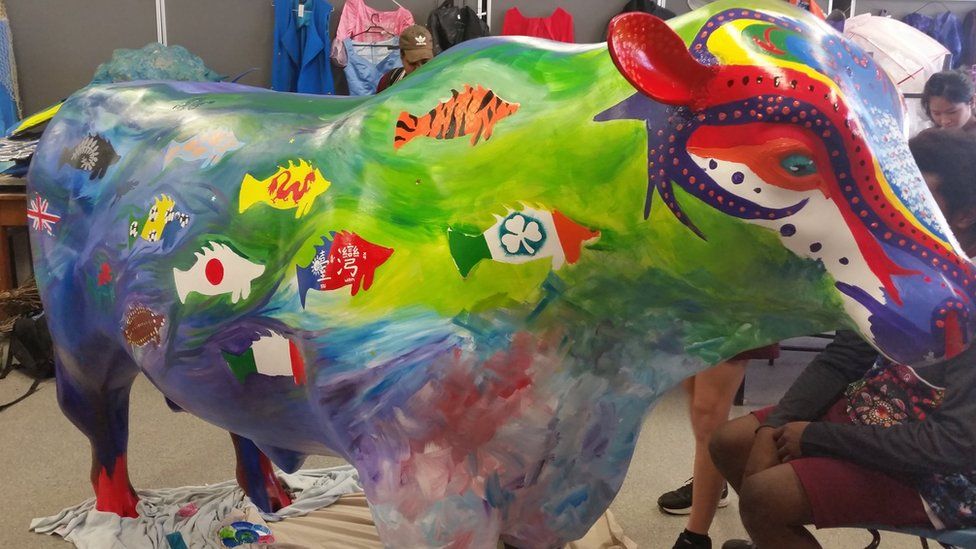 A colourful bull statue that has country flags in the shape of fish painted on it