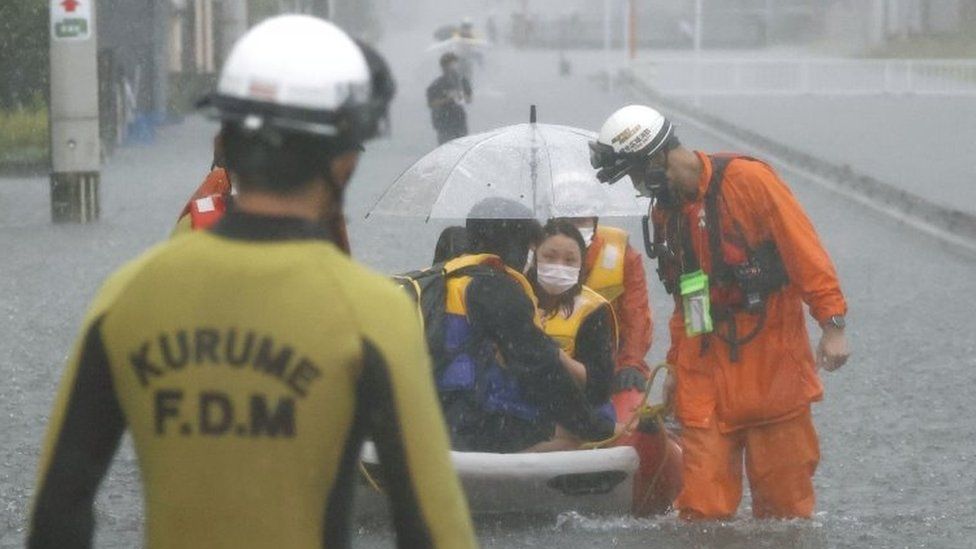 Firefighters transport stranded residents on a boat in a road flooded by heavy rain in Kurume, Fukuoka prefecture,