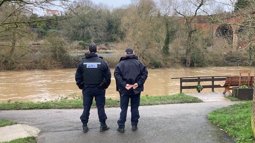 Two police officers stand next to a river