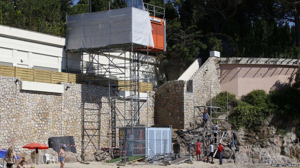 People sit and stand by the water as workers disassemble an elevator on the public beach near the Saudi King"s villa in the Golfe-Juan seaside resort in Vallauris, southeastern France, on August 3, 2015.