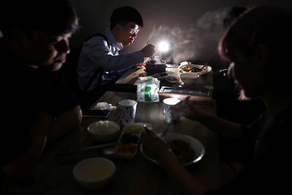 People eat using the light from a phone while experiencing a blackout due to an outage at a power plant, in Taipei, Taiwan, 13 May 2021.