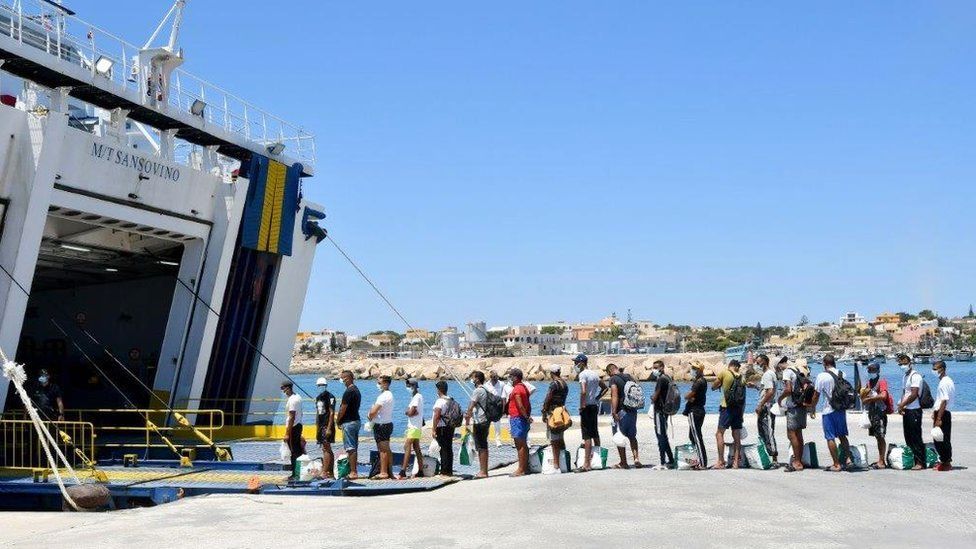 Migrants escorted by police queue to board on a tourists ferry boat to Porto Empedocle onthe Italian island of Lampedusa on 29 July 2020