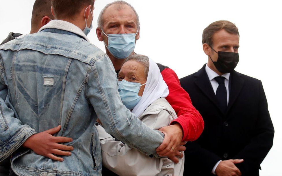 French President Emmanuel Macron (R) stands next to French aid worker Sophie Petronin (C) who is welcomed by her family after suspected jihadist hostage-takers freed the 75-year-old from nearly four years of captivity in Mali upon her arrival at the Villacoublay military airport near Paris on October 9, 2020.