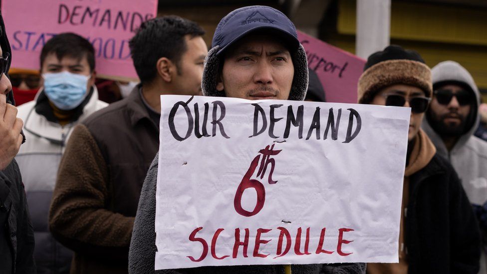 A man holds up sign demanding implementation of the sixth schedule