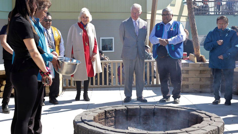 Prince Charles and Camilla stand around a fire pit