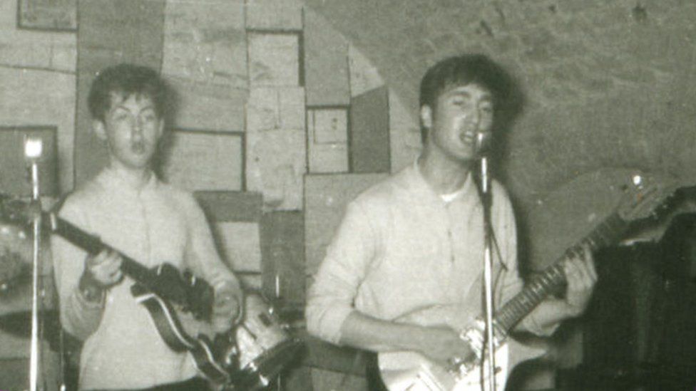 John Lennon and Sir Paul McCartney at the microphone, with George Harrison on guitar and a partially obscured Pete Best, the group's original drummer