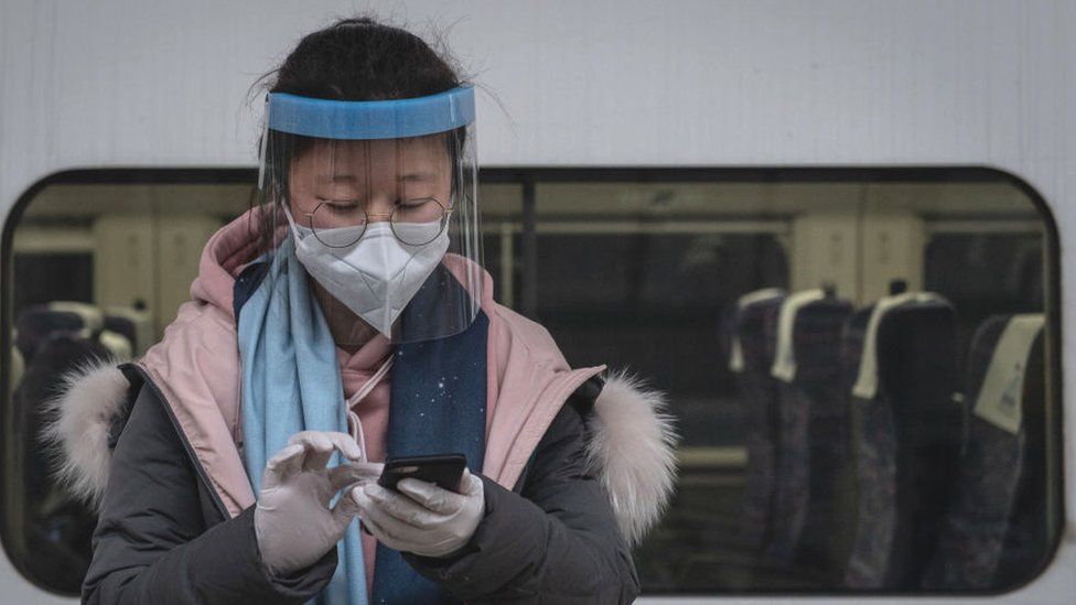 A masked traveler sends a message on her phone on the platform at Hankou Railway Station in Wuhan