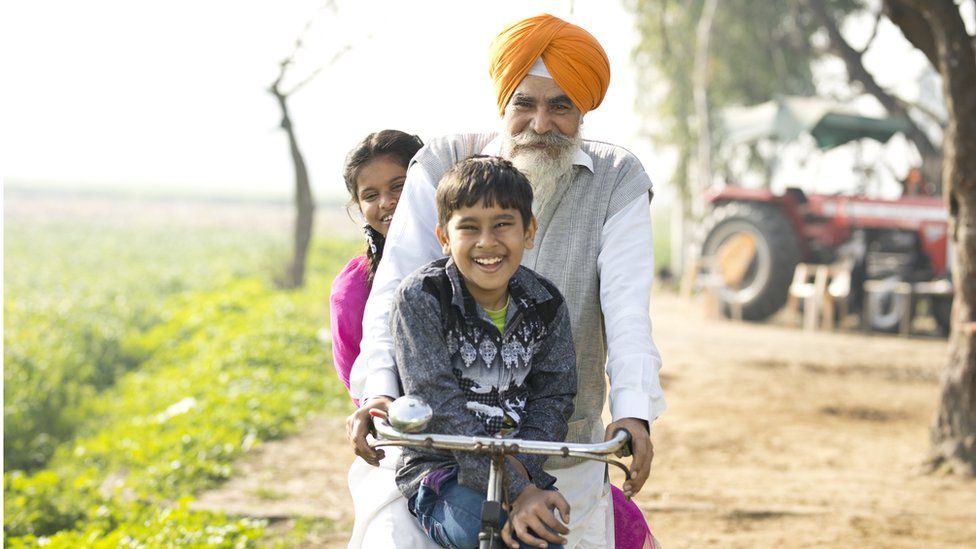A man with a grey beard and a turban on a bike with two young children