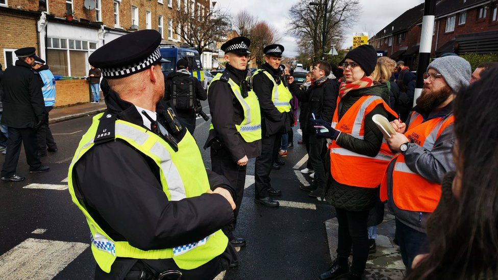 Met Police Officers stand in front of people on the road.