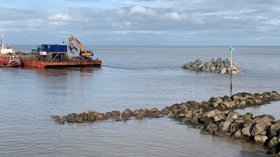 A digger placing rocks in the sea close to the Somerset coast at Watchet