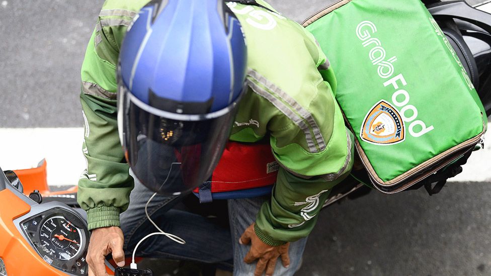 A Grab motorcycle rider checks his mobile phone in Bangkok, Thailand
