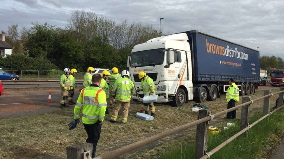 Firefighters clean up a diesel spill following a lorry crash - around 6 or 7 fighfighters are pictured in high vis clothing