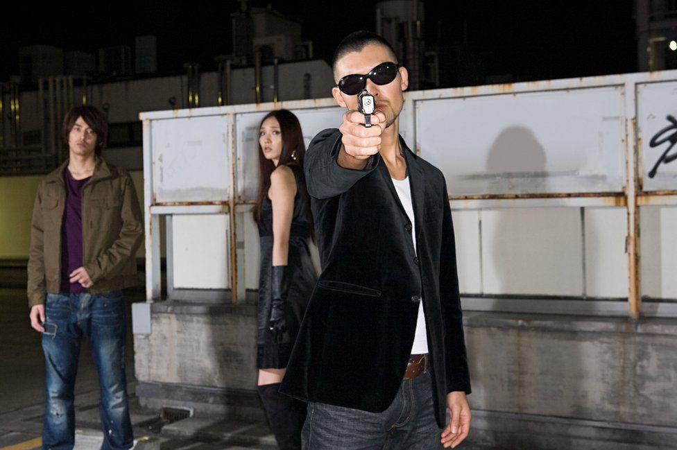 Japanese man points gun at camera
