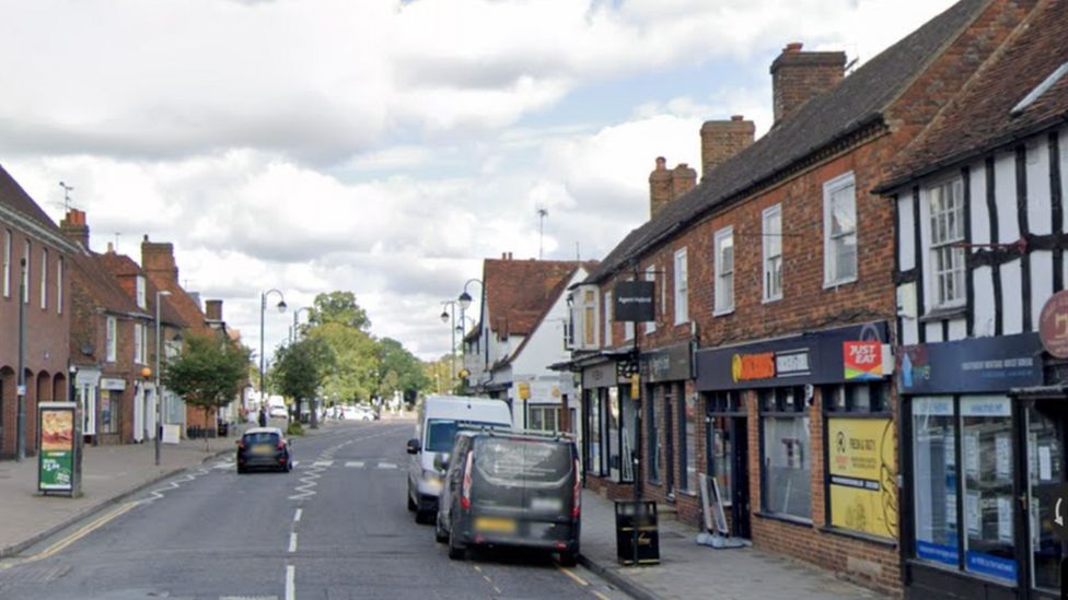 Stevenage High Street. There are shops on both sides and cars parked on the right side of the pavement