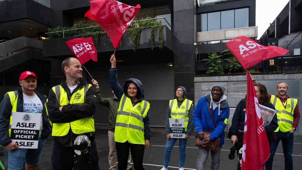 Члены Aslef размахивают флагами во время забастовки на железнодорожной станции Юстон