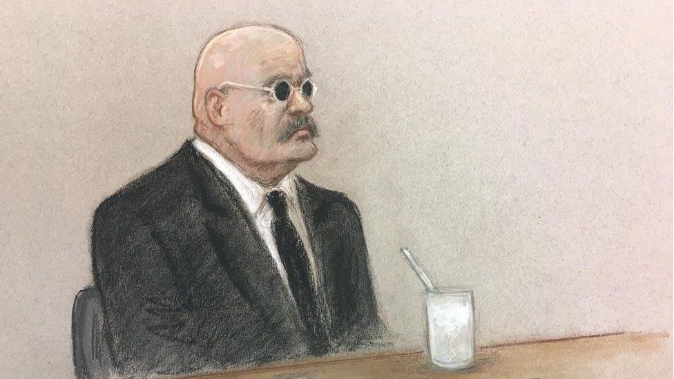 A court sketch of prisoner Charles Bronson shows him in black suit and tie, wearing a white shirt. He is wearing a pair of white glasses with black lenses.
