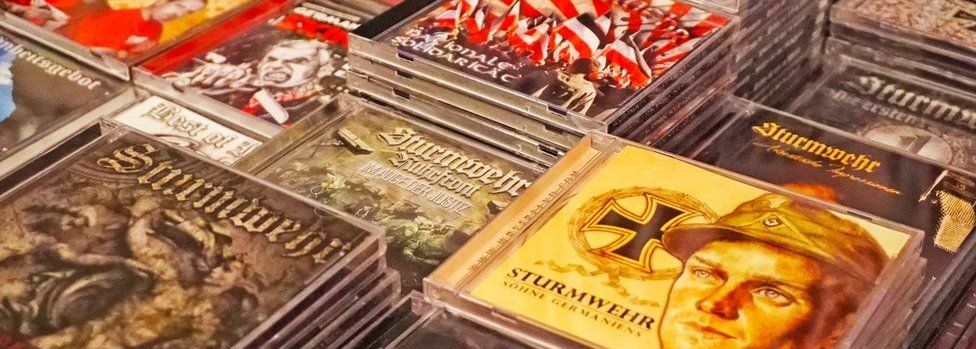 Stacks and stacks of CDs are pictured, many from the band Sturmwehr, with military images and flags visible on some cover art