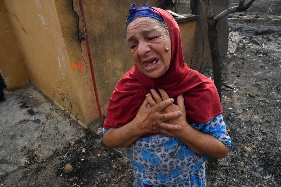 An elderly Algerian woman reacts in front of the ruins of her home, destroyed in a wildfire in the city of el-Kala.