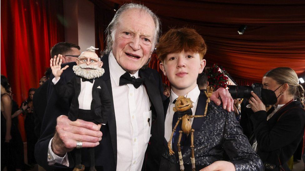 Actors David Bradley and Gregory Mann pose on the champagne-colored red carpet during the Oscars arrivals at the 95th Academy Awards