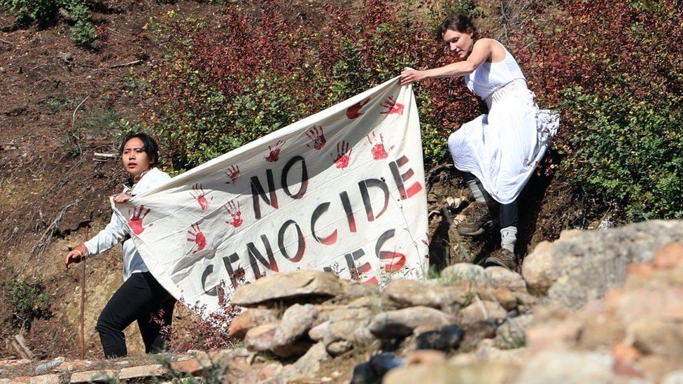 Two female protesters holding a banner saying 'No Genocide Games' with red hand prints on