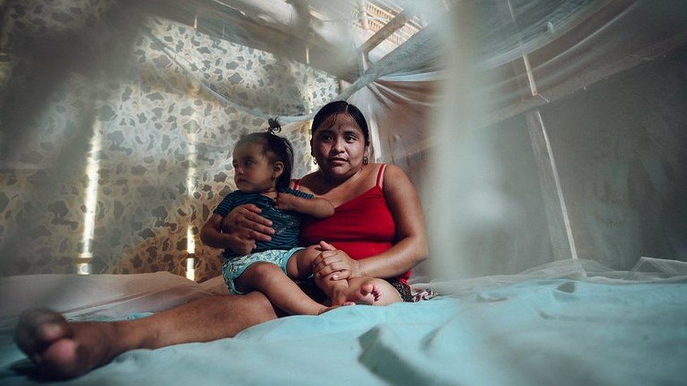 A woman sits underneath mosquito net with her child in Belize