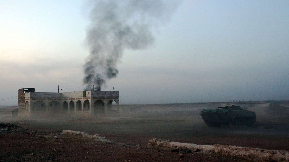 A picture taken on 17 October 2015 shows smoke billowing from a building as a rebel tank moves through Mount Azzan area, outside Aleppo