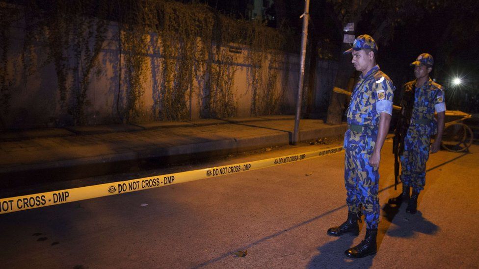 Police officers stand guard at the site where an Italian charity worker has died after being shot by attackers in Dhaka