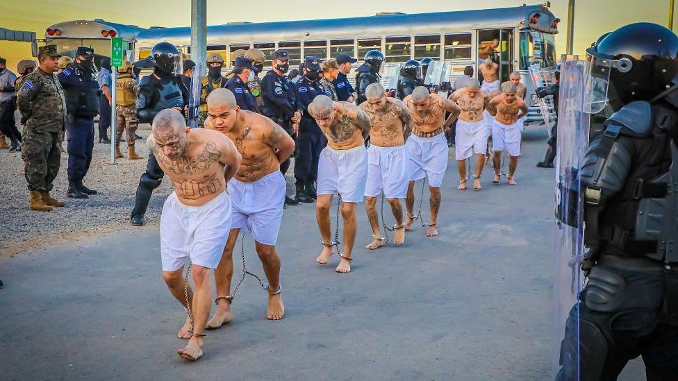 Agentes penitenciários observam membros de gangues enquanto descem de um ônibus em sua chegada depois que 2.000 membros de gangues foram transferidos para o Centro de Confinamento de Terrorismo