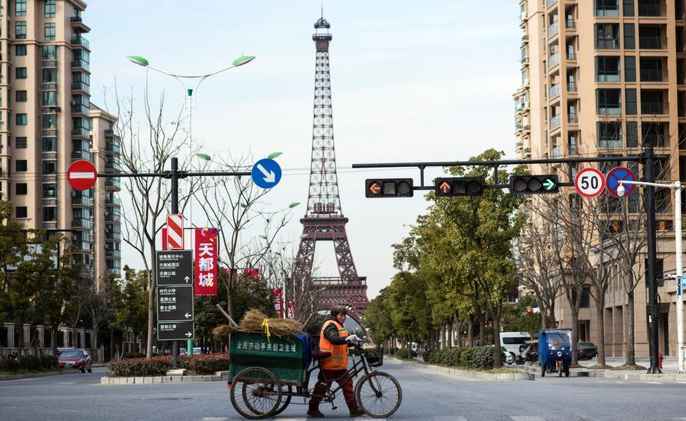 A street cleaner pushes a cart across a junction in front of a replica Eiffel Tower in Tianducheng, a luxury real estate development in Hangzhou in Zhejiang province on 26 January 2016.