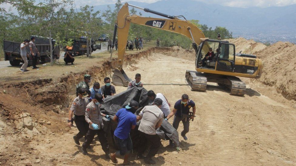 Indonesian security forces carry the body of a victim of the earthquake and tsunami into a mass grave in Palu, Central Sulawesi, Indonesia October 1, 2018