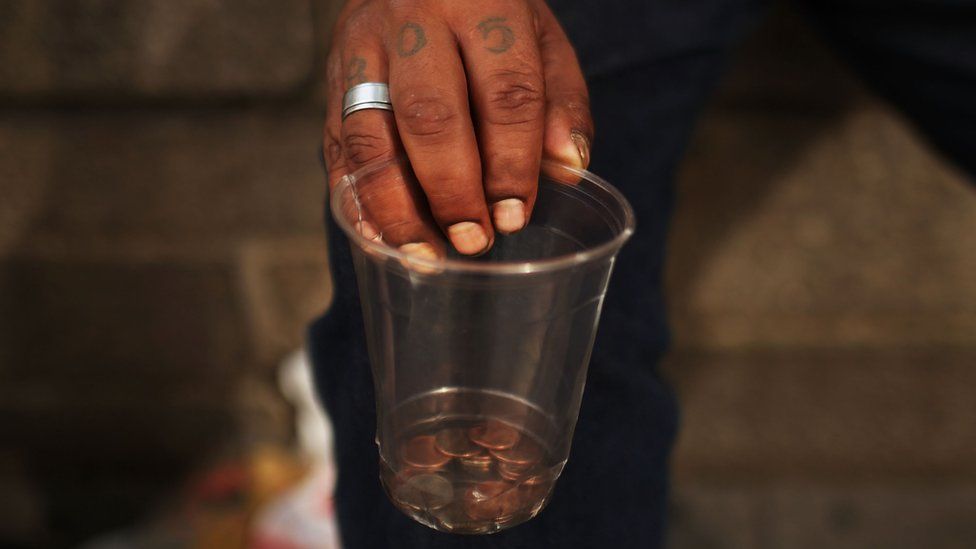 A homeless man holds a cup with coins