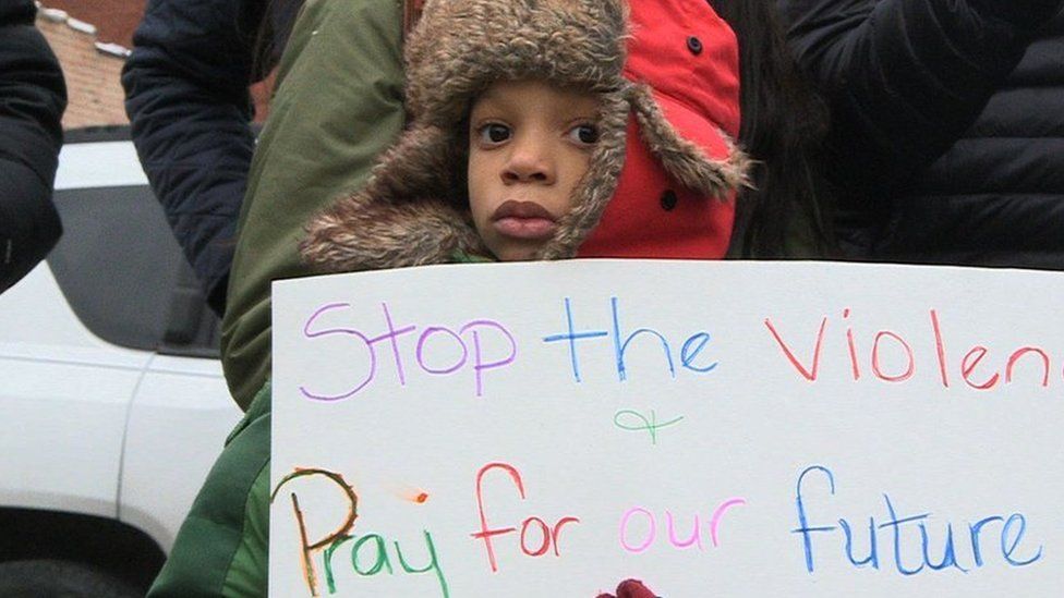 Child at a demo with a banner that says "Stop The Violence"