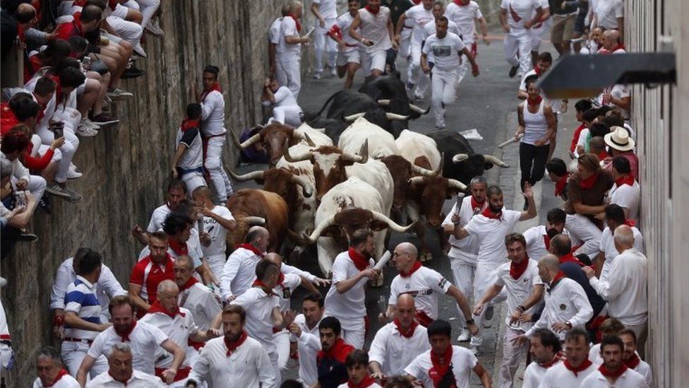 Runners try to avoid bulls of the Puerto de San Lorenzo bull ranch as they run down a street during the traditional San Fermin bull run