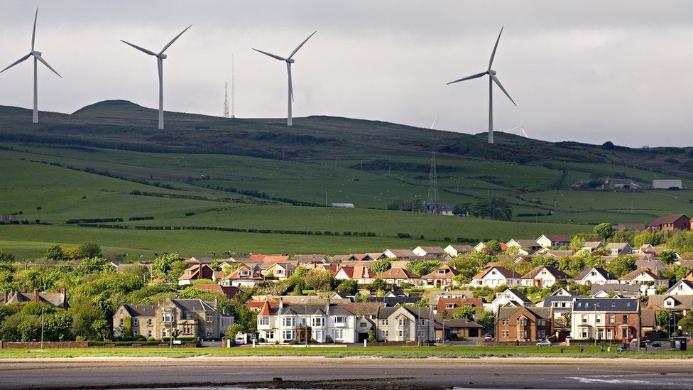 Wind turbines in background, and housing estate on edge of field by sea in foreground