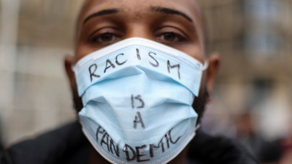 A protester wears a mask saying "racism is a pandemic" at a BLM demonstration in Birmingham, England