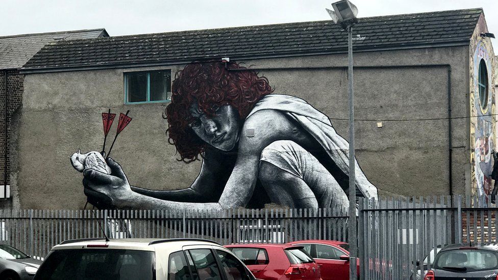 A huge mural of a woman crouching holding a bird with arrows in it.