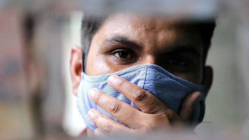 A man wearing a face mask looks on from a gate in Baramulla, Jammu and Kashmir, India on 12 September 2020.