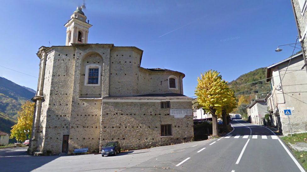 A Google Street view image of the town of Acquetico, showing an old stone church and a single pedestrian crossing
