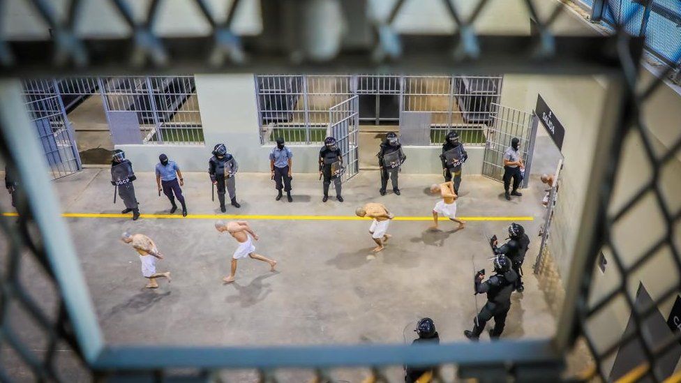 Agentes penitenciários observam membros de gangues enquanto são processados ​​em sua chegada, depois que 2.000 membros de gangues foram transferidos para o Centro de Confinamento de Terrorismo