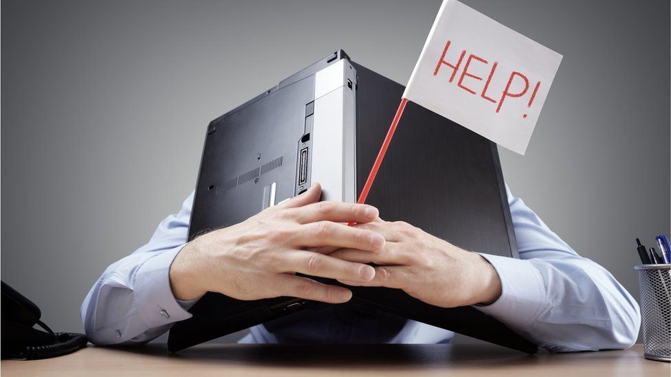 Man hiding under a laptop with a help sign