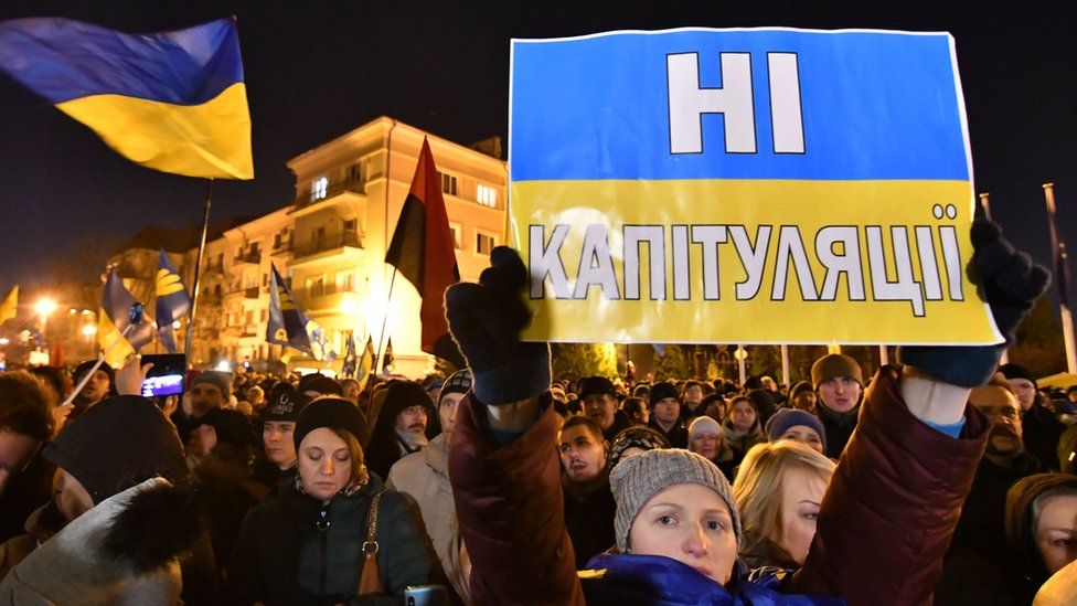 A woman holds a sign at a protest in Kyiv reading "no capitulation" in Ukrainian