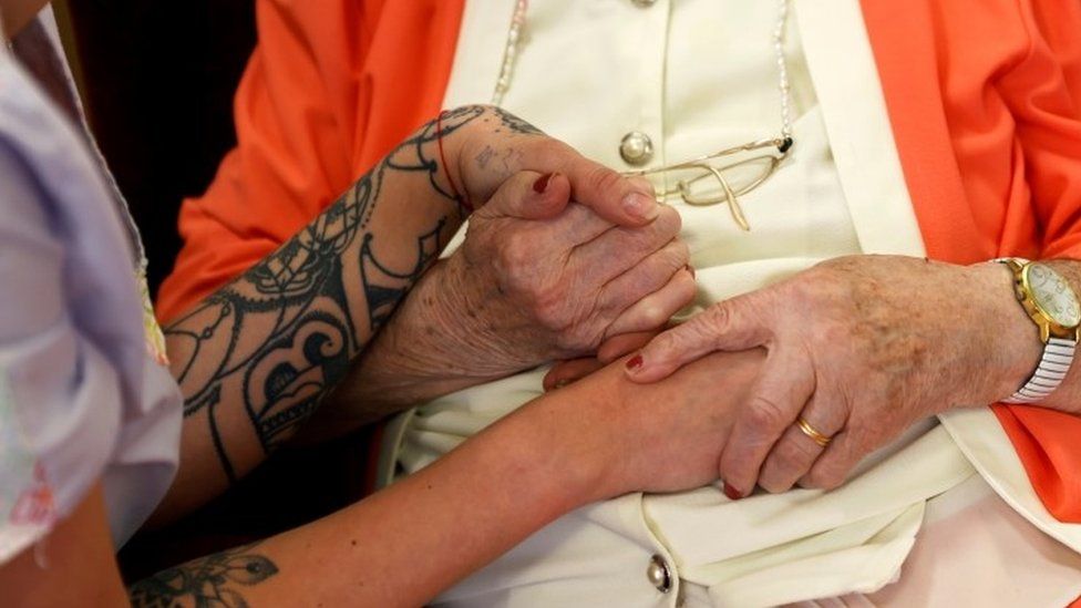 Care home worker holds resident's hand