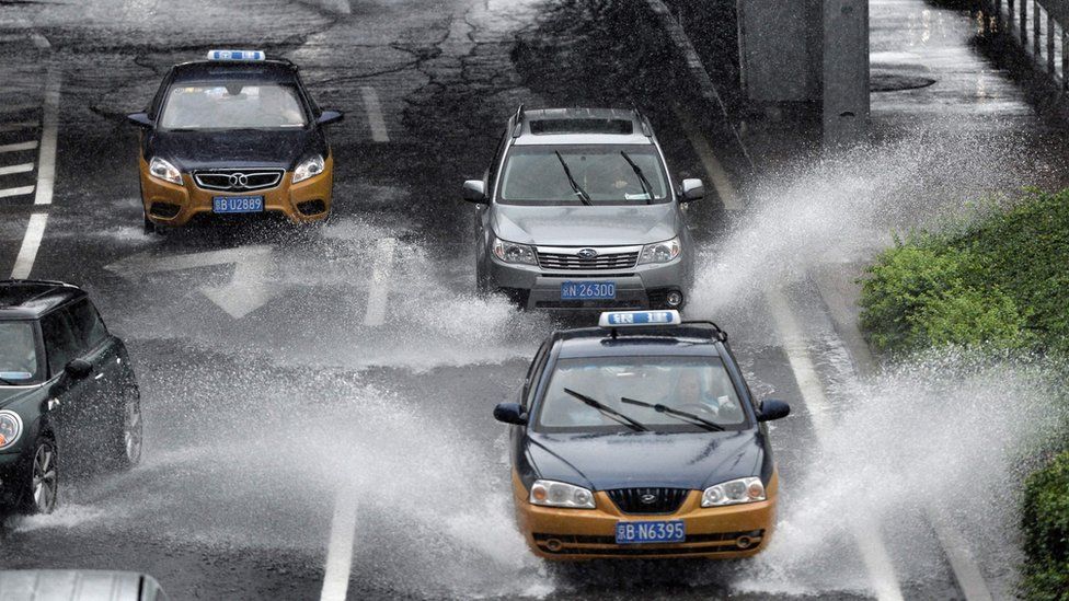 Taxis and cars commute on a flooded road in Beijing on July 20, 2016.